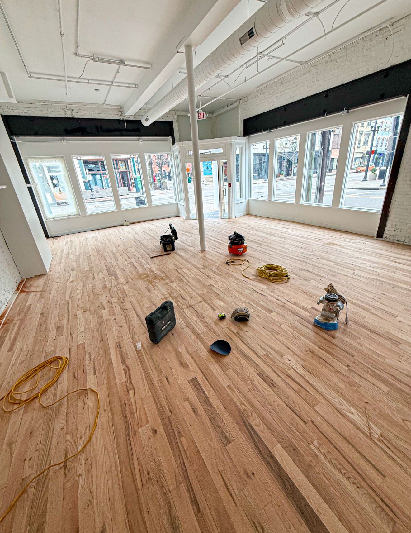 Empty room with large windows and newly installed wooden flooring, featuring various construction tools scattered around.