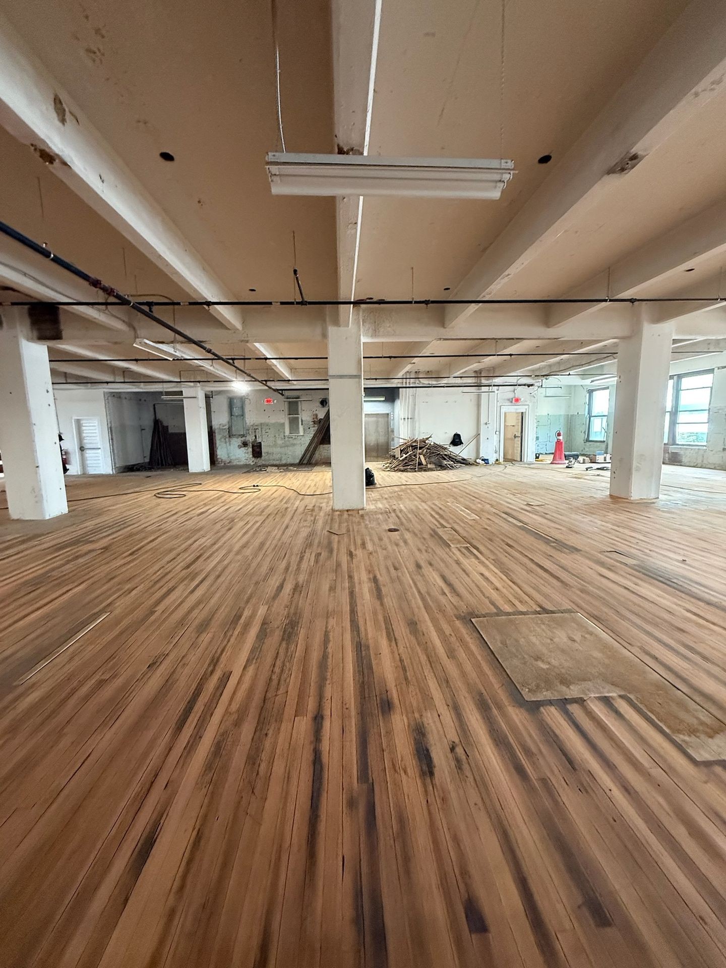 Spacious industrial space with wooden floors, exposed beams, and large windows, under renovation.